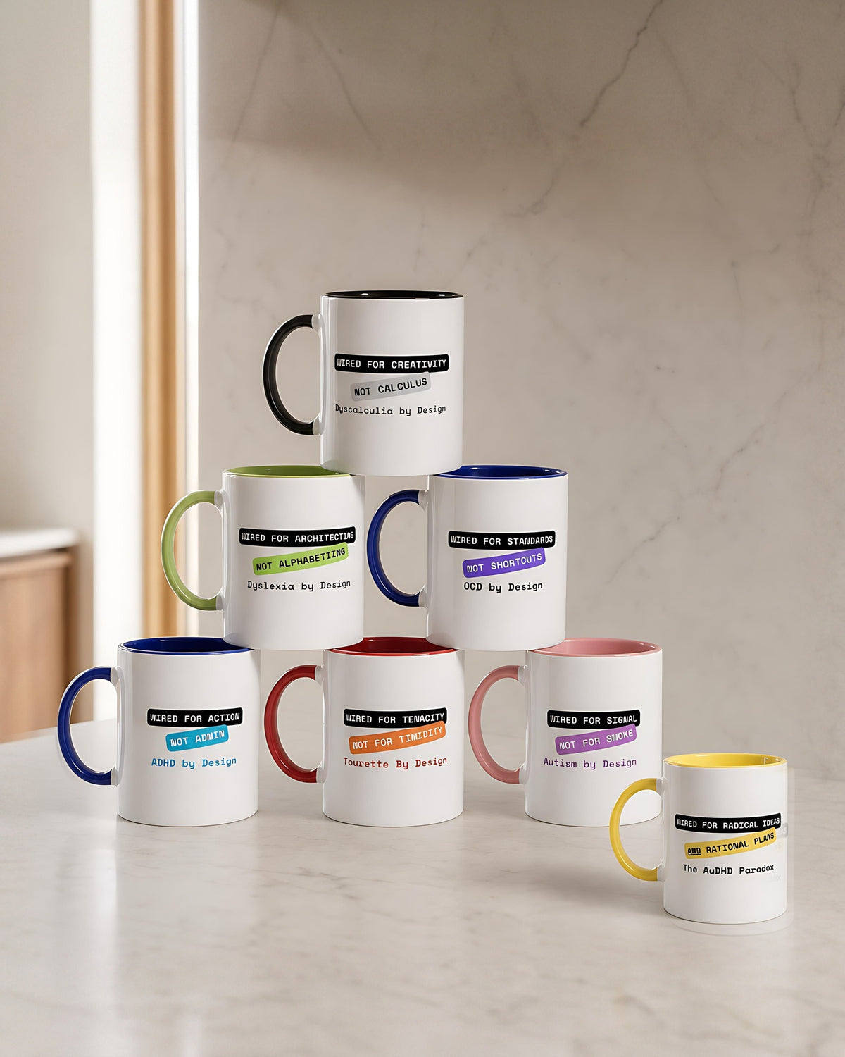 Seven By Design mugs stacked in a pyramid on marble, with the yellow AuDHD Paradox mug standing apart