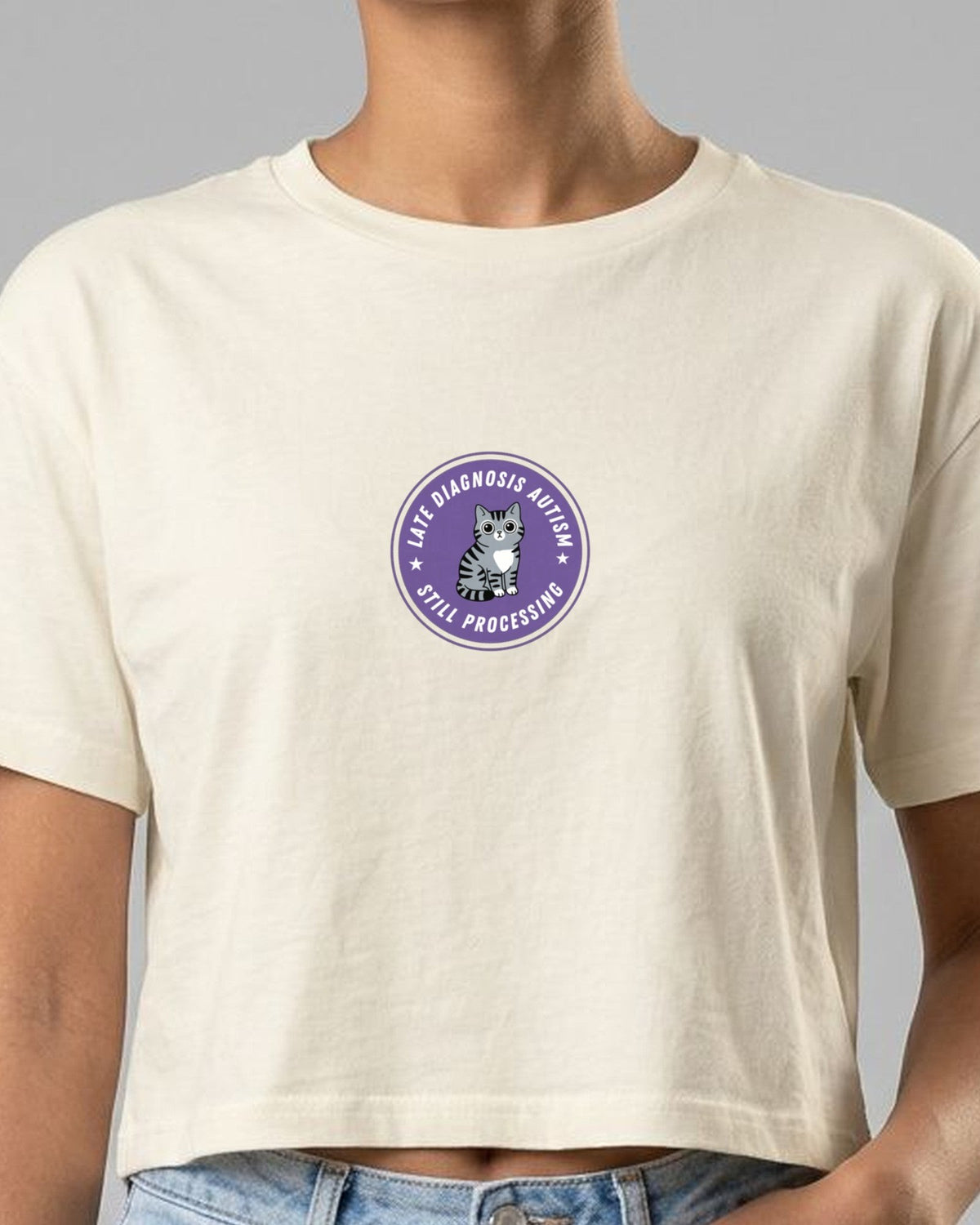 Woman in a cream crop top with the purple Late Diagnosis Autism, Still Processing cat badge