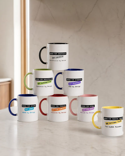 Seven By Design mugs on a pale marble worktop: a pyramid for ADHD, Tourette, Autism, Dyslexia, OCD and Dyscalculia, with the yellow AuDHD Paradox mug in front