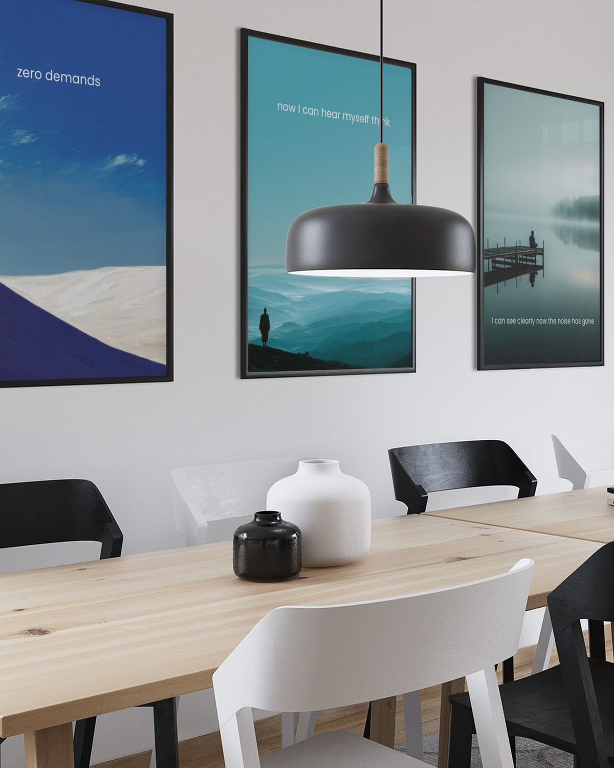 Three calm landscape prints above a pale wooden dining table with black pendant lights