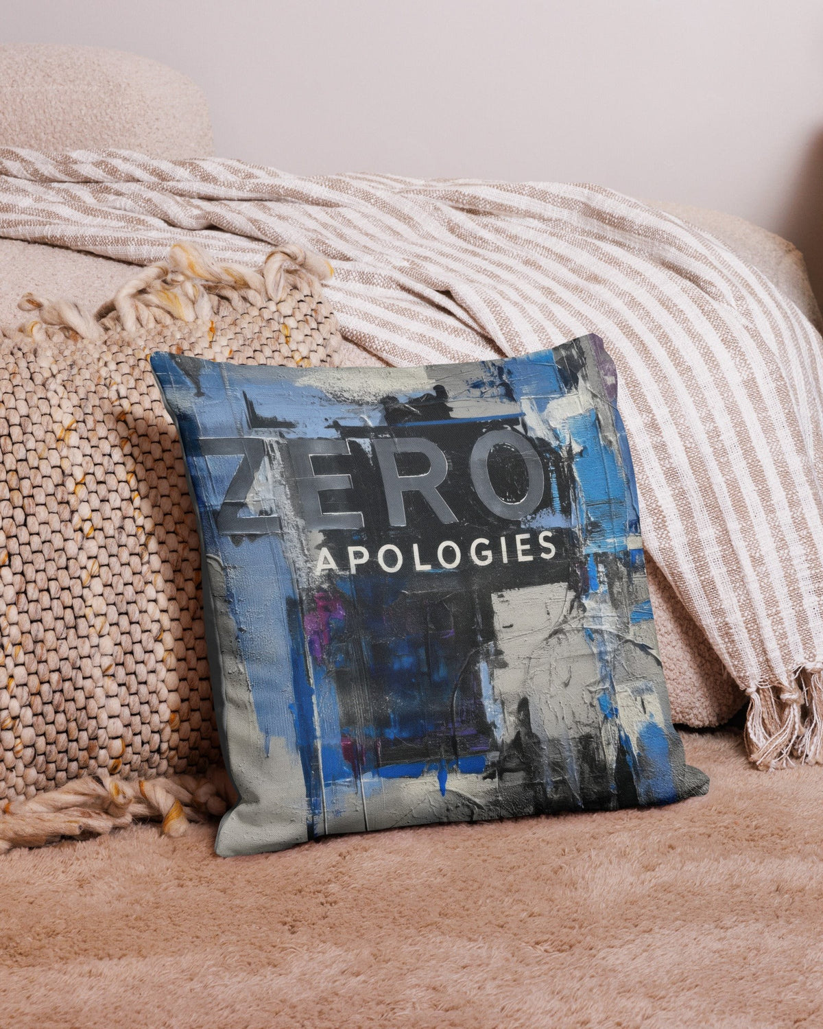 Blue and grey Zero Apologies graffiti cushion propped against a beige sofa with a striped throw