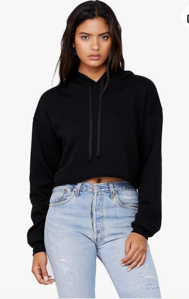 A woman modeling a black cropped long-sleeve hoodie with drawstrings, paired with light-wash distressed jeans, against a plain white background.