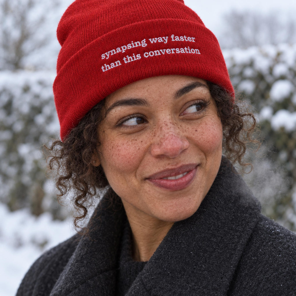 Woman in a red ribbed beanie embroidered with the words synapsing way faster than this conversation