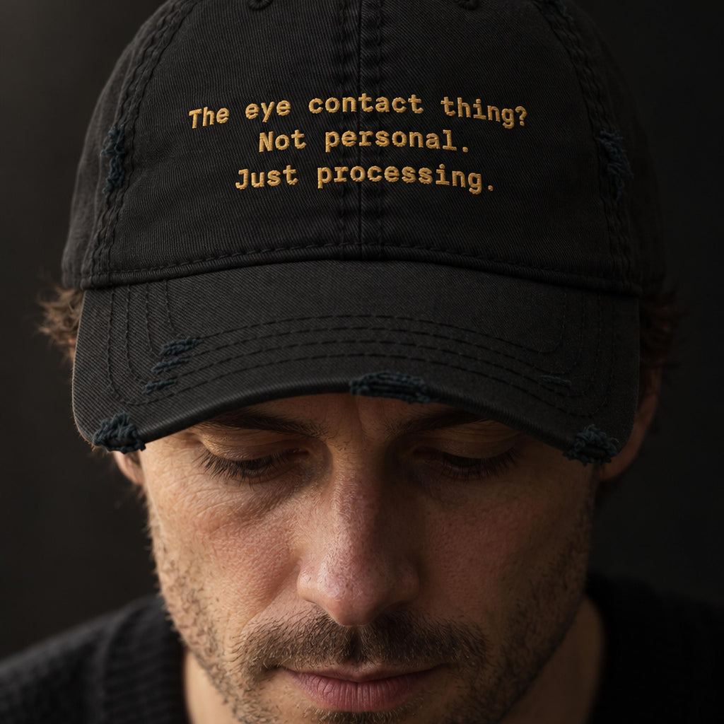 Man in a black distressed dad hat embroidered with the words the eye contact thing, not personal, just processing