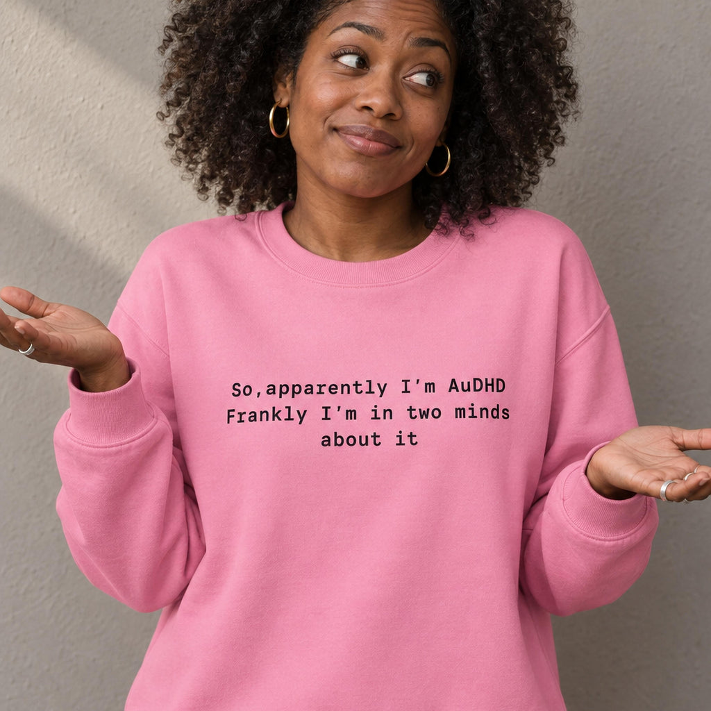Woman shrugging in a pink organic sweatshirt printed with the words so apparently I am AuDHD, frankly I am in two minds about it