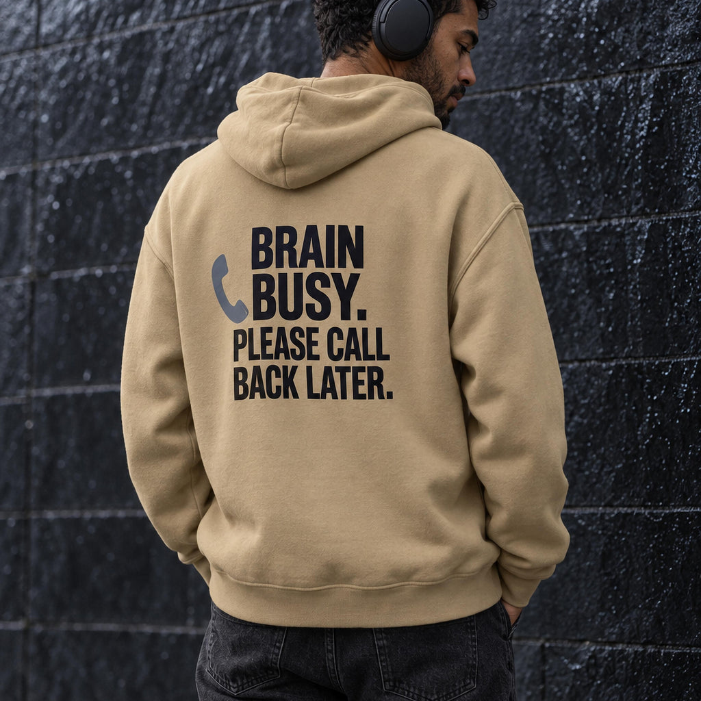 Man seen from behind in a sand-coloured oversized hoodie back-printed with the words brain busy, please call back later