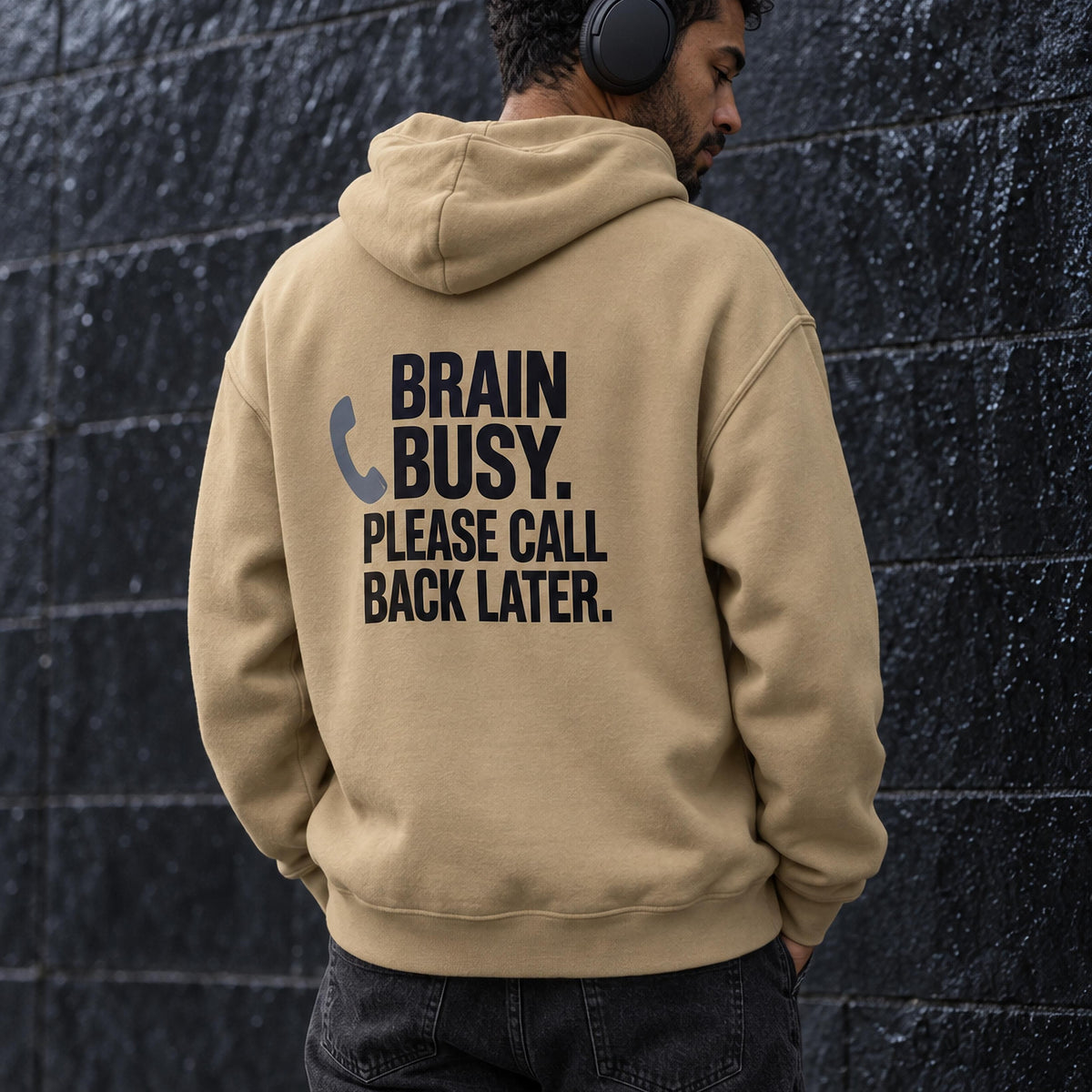 Man seen from behind in a sand-coloured oversized hoodie back-printed with the words brain busy, please call back later