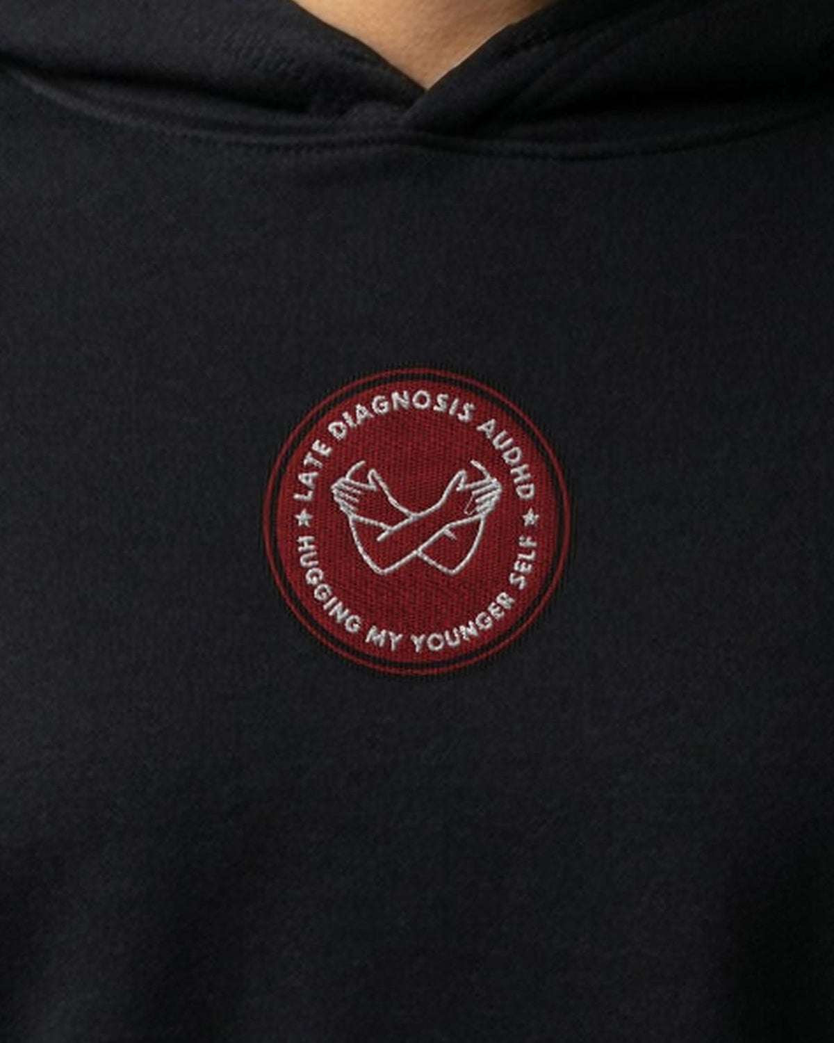 Hugging ... AuDHD embroidered crop hoodie in Black, worn, close-up of the chest design