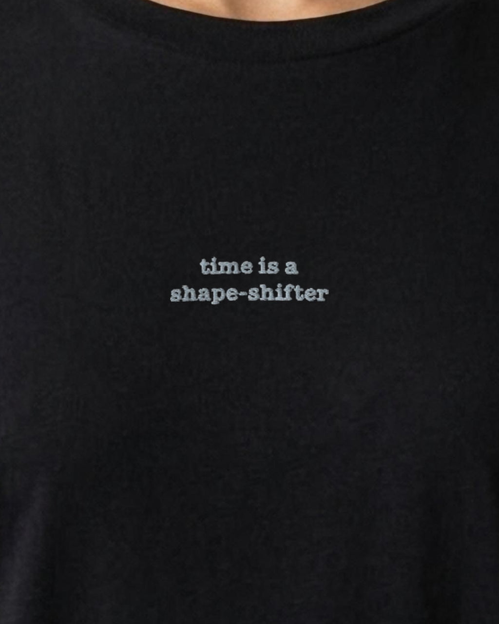 Time Is a Shape-Shifter embroidered organic tee in Black, worn, close-up of the chest embroidery